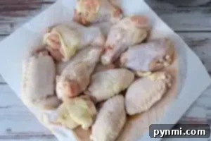 A collection of raw chicken wings and drumsticks are laid out on a white paper towel on a rustic, white wooden table. The fresh chicken pieces are ready for preparation or cooking, and would be perfect as air fryer chicken wings when seasoned with a touch of baking powder.