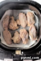 Firecracker chicken wings with seasoning sizzle in an air fryer basket lined with parchment paper.