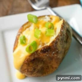 Crockpot baked potatoes topped with cheese sauce and chopped green onions on a white plate with a fork.