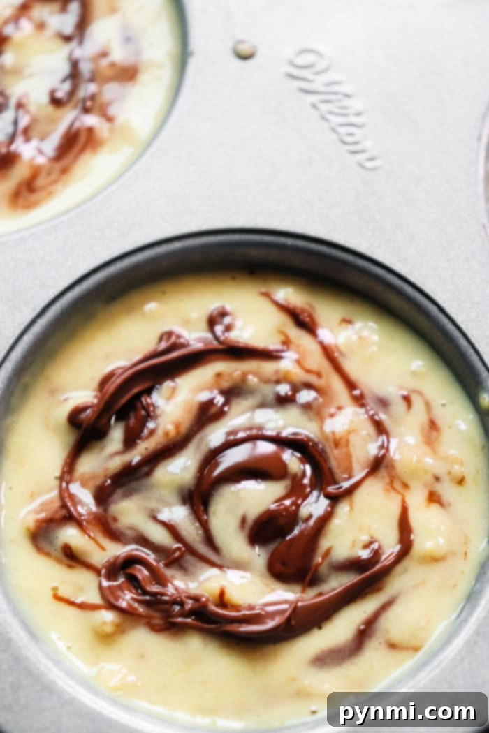 Nutella Swirl Banana Muffins 6 Close-up of golden banana muffin batter with luscious Nutella swirls, perfectly set in a baking tin, ready for the oven to transform into a delicious breakfast or snack.