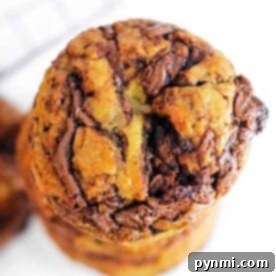 Close-up of a stack of Banana Nutella Muffins with visible chunks of chocolate on a white background, tempting enough to rival the allure of freshly baked Banana Nutella Muffins.
