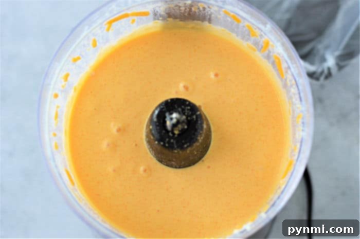 Whip Up Perfect Velveeta Cheese Sauce Every Time 4 Blended cheese sauce mixture, reminiscent of a delectable Velveeta cheese sauce, swirled in a food processor bowl, showcasing its smooth texture.