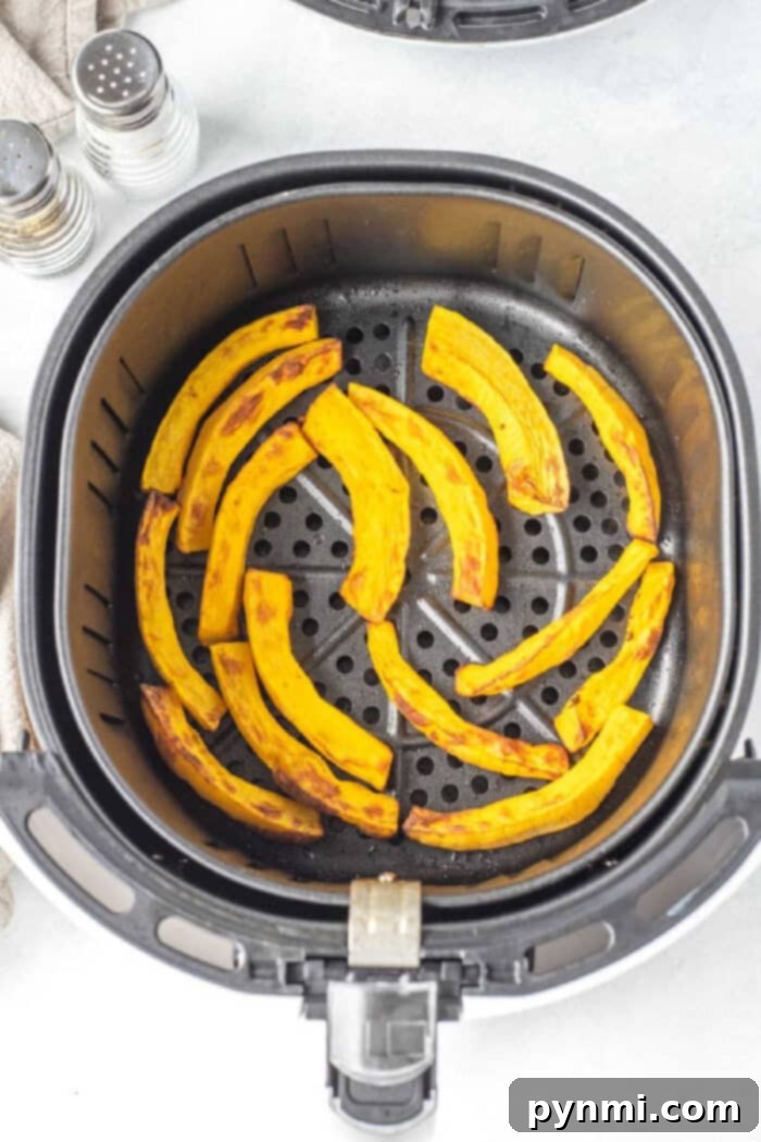 Air Fryer Roasted Pumpkin 6 Curved slices of air fryer pumpkin in a basket, with salt and pepper shakers nearby.