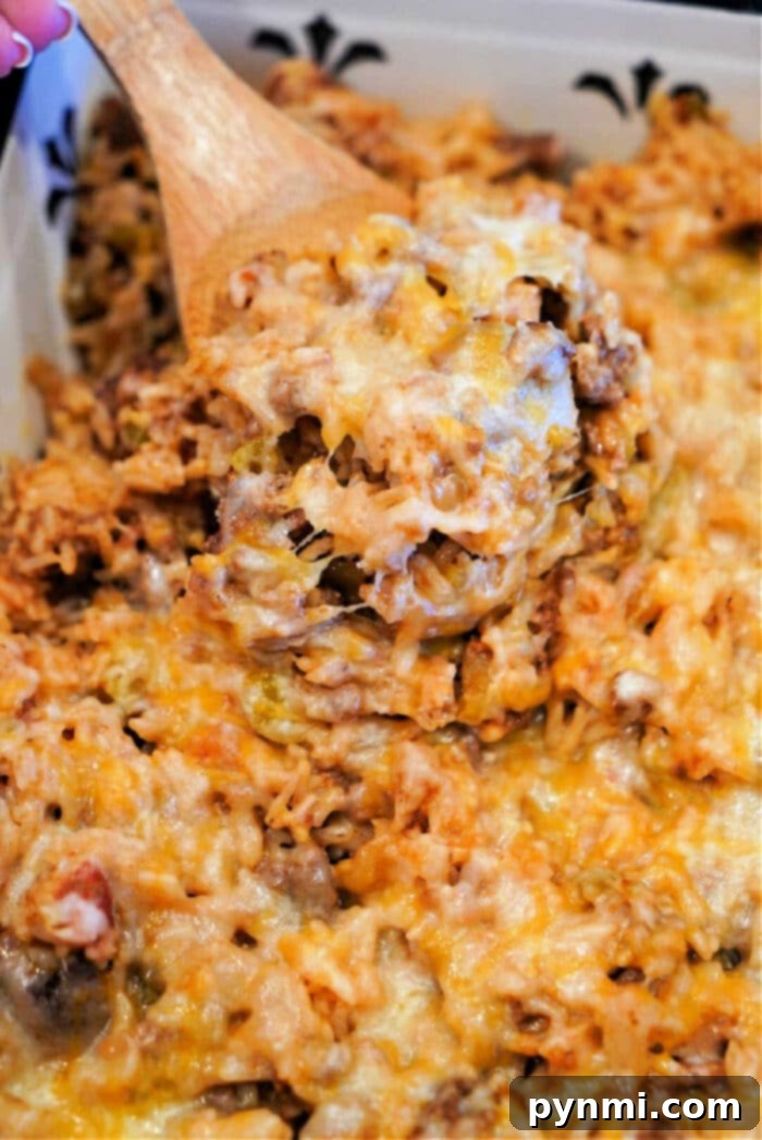 A bubbling cheesy hamburger and rice casserole in a white baking dish, fresh out of the oven, with a spoon ready to serve.