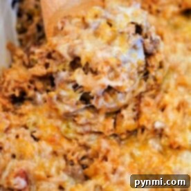 A spoon serving a cheesy baked hamburger and rice casserole with ground meat and pasta from a dish.