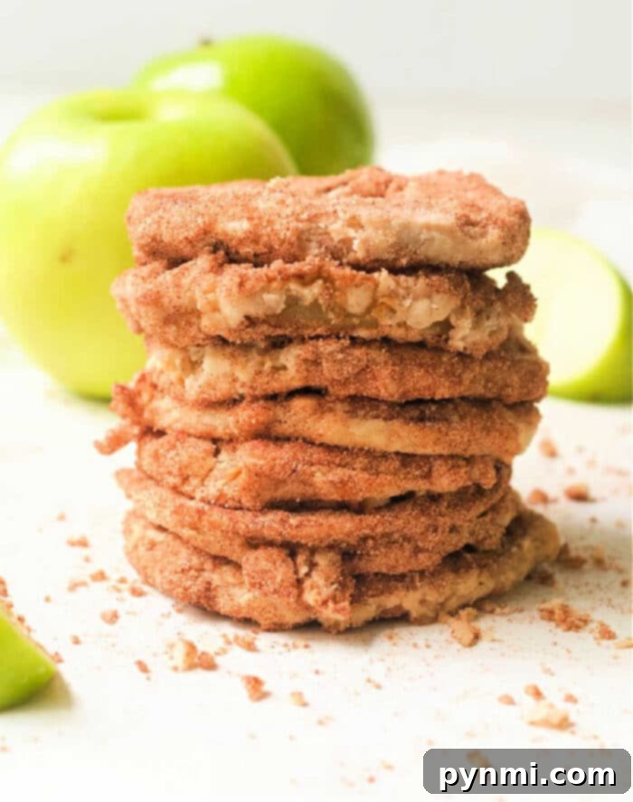 A stack of crispy fried air fryer apple slices sits invitingly, with crisp green apples in the background. Each bite promises a delightful crunch and sweetness, a perfect air fryer apple snack.