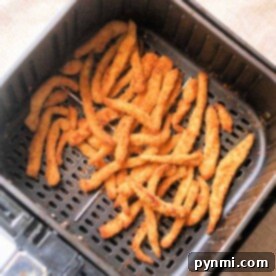 Golden chicken fries in an air fryer basket rest on a beige surface, promising a crispy delight.