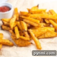 Golden baked turnip fries on parchment paper, crisped to perfection in the air fryer, with a small cup of ketchup in the background.