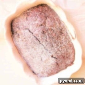 A freshly baked loaf of chocolate gingerbread bread in a scalloped baking dish, dusted with flour.