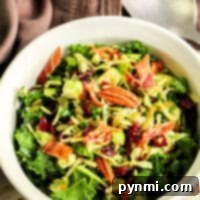A white bowl of leafy salad with Brussels sprouts, pecans, cranberries, and bacon bits sits on a tablecloth with a spoon nearby.