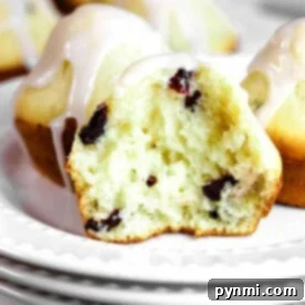 A healthy cranberry muffin with yogurt and glaze, cut in half, sits invitingly on a white plate, revealing its moist interior and vibrant cranberry pieces.