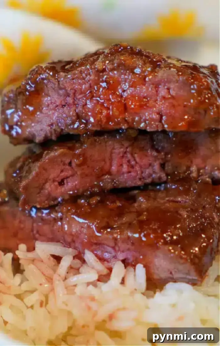 A close-up shot of three glistening slices of barbecued beef, stacked neatly on a bed of fluffy white rice. The beef, likely prepared using an air fryer beef recipe, shows a tender, moist interior with tantalizingly charred edges. The background is softly blurred, hinting at a colorful, patterned tablecloth.