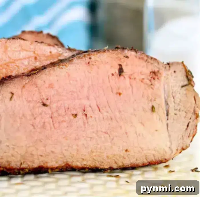 A close-up view of a thick, perfectly cooked slice of beef, displaying a beautiful pink interior indicating medium-rare doneness, and a slightly charred outer edge. This succulent cut is an excellent example of a successful air fryer beef recipe. The background is softly blurred, featuring a blue and white striped cloth and a simple surface.