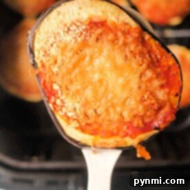 A close-up of a slice of air fryer eggplant parm, topped with rich tomato sauce and melted cheese, resting perfectly on a spoon.