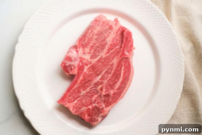 Air Fryer Lamb Chops: Your New Favorite Dinner 4 A succulent raw lamb shoulder chop rests on a white plate with a textured rim, much like you would present perfectly cooked lamb chops from the air fryer.