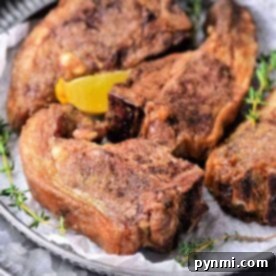 Air Fryer Lamb Chops: Your New Favorite Dinner 7 Four perfectly seasoned lamb chops, cooked to tender perfection in an air fryer, rest on a plate adorned with a lemon wedge and fresh thyme sprigs.