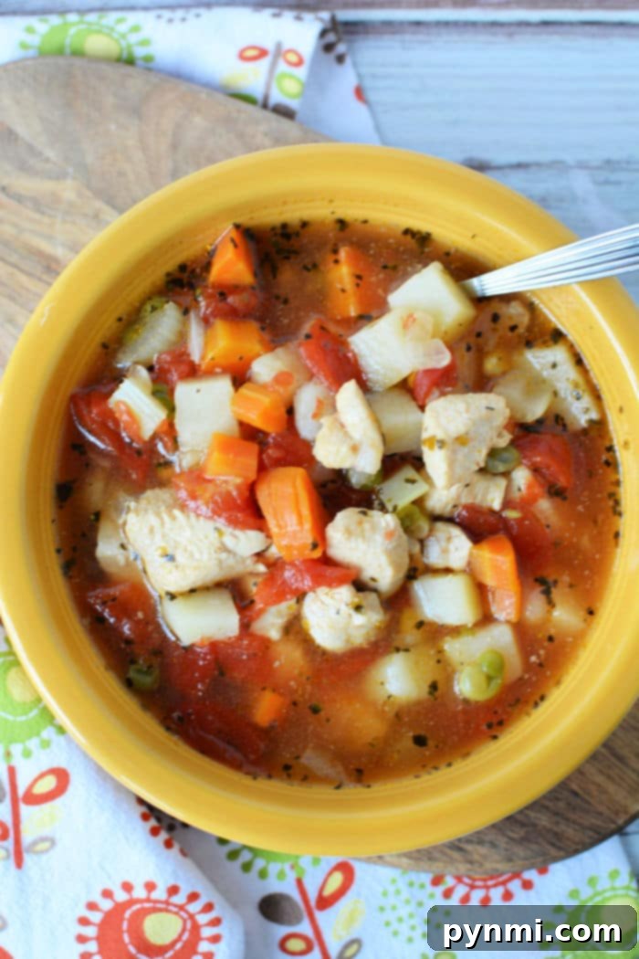 A vibrant yellow bowl of Instant Pot chicken vegetable soup, brimming with golden diced potatoes, bright orange carrots, fresh green peas, and juicy red tomatoes. A spoon rests invitingly in the bowl, which sits on a subtly patterned cloth, ready to be enjoyed.