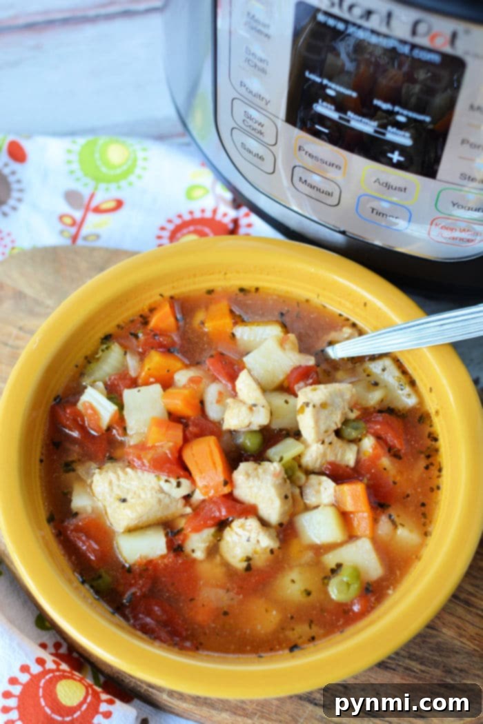 A charming yellow bowl brimming with hearty Instant Pot chicken vegetable soup. The soup features succulent pieces of tender chicken, soft diced potatoes, vibrant carrots, sweet peas, and juicy tomatoes. A spoon is nestled within the bowl, while an Instant Pot rests softly in the background on a colorful floral patterned cloth, highlighting the homemade comfort of the meal.