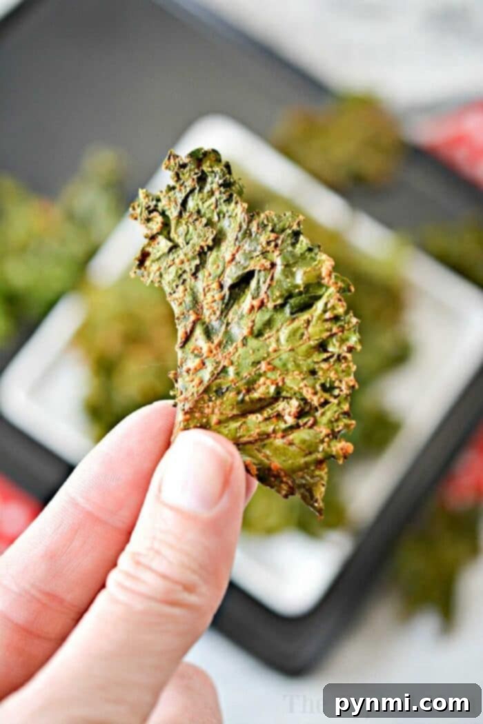 An overhead shot of two hands reaching for a fresh batch of crispy kale chips on a white baking sheet, emphasizing their irresistible appeal.