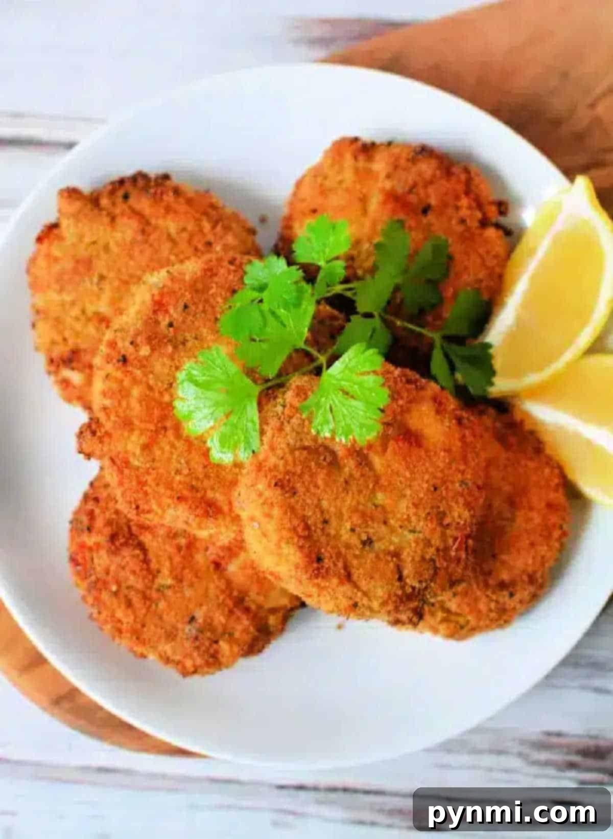 Crispy Air-Fried Crab Cakes 2 Five golden brown Air Fryer Crab Cakes garnished with cilantro and lemon wedges on a white plate.