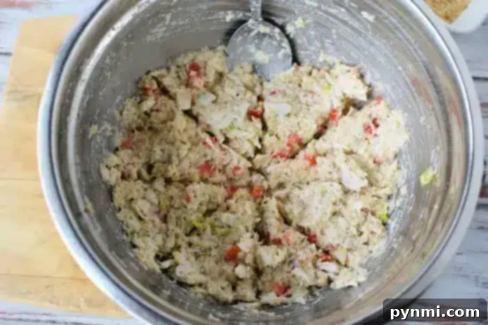 A metal mixing bowl containing a mixture of various chopped ingredients, likely including bread crumbs, bits of red and green vegetables, and a creamy binder for Air Fryer Crab Cakes. 