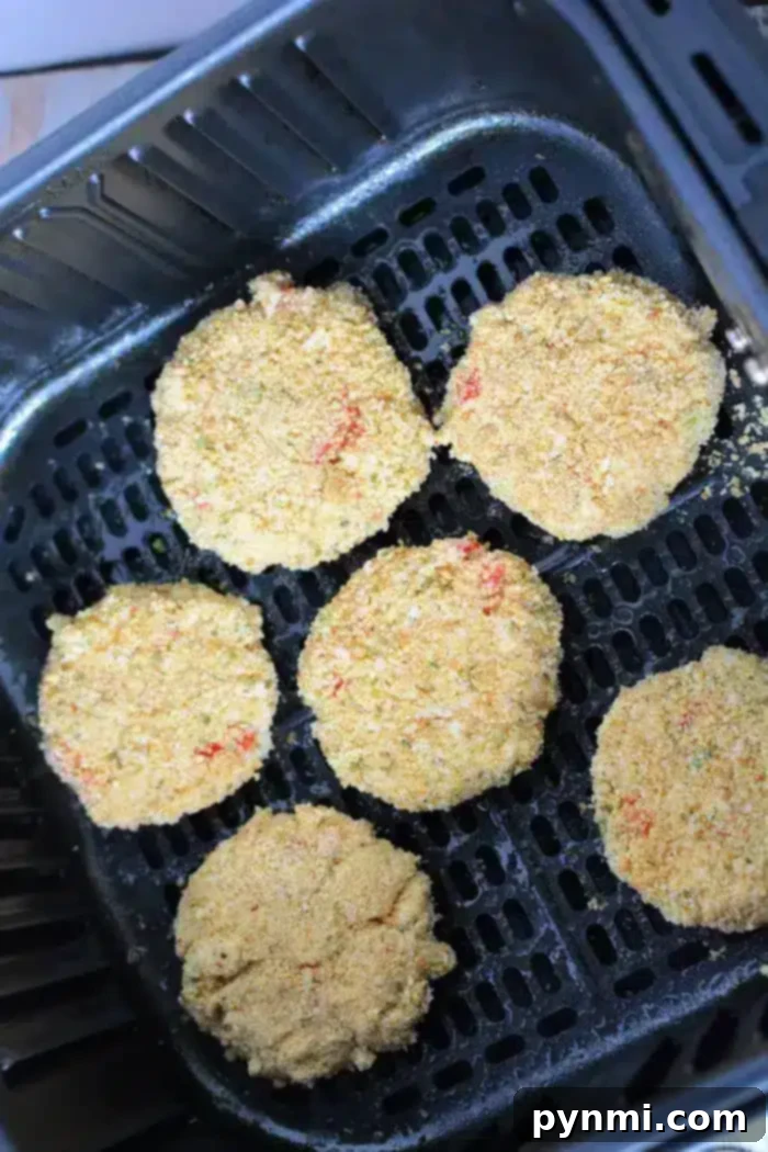 Crispy Air-Fried Crab Cakes 6 Five breaded and round air fryer crab cakes are placed in the basket, ready for cooking. The patties appear to be evenly spaced and have a golden-brown crumb coating. The black air fryer basket, with its perforated base, sets the stage for a perfect crisp.