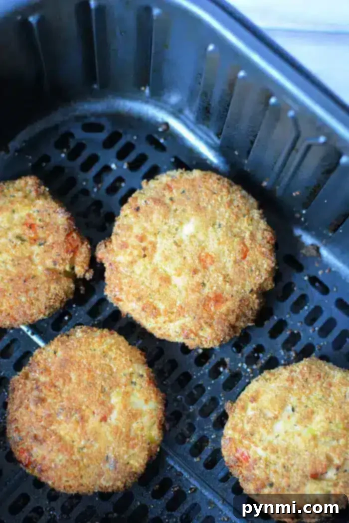 Crispy Air-Fried Crab Cakes 8 Four breaded and fried crab cakes are placed inside an air fryer basket. The patties are golden brown with a crispy exterior. The air fryer basket has a dark, nonstick surface with visible grill lines.