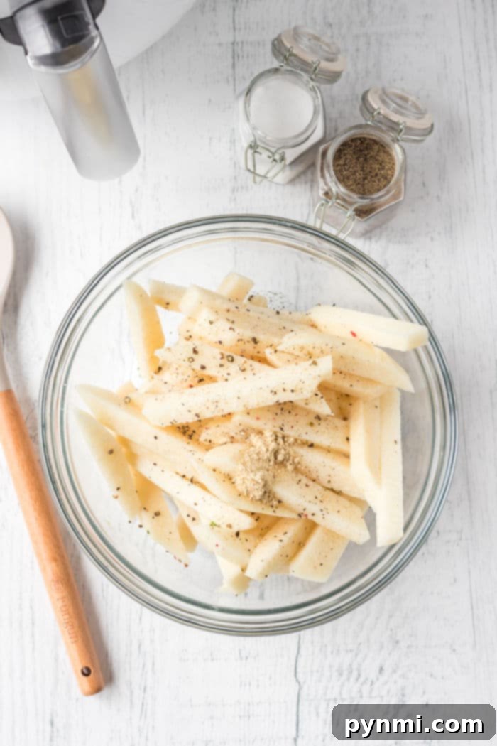 Refreshing Jicama Sticks 3 A glass bowl holds air fryer jicama fries, seasoned to perfection with spices and herbs, while a wooden spoon and spice jars rest nearby.