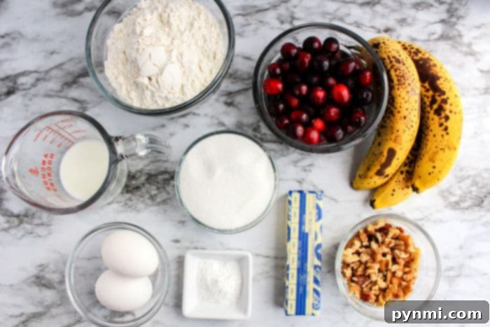 A medley of baking ingredients spread across a marble surface: ripe bananas, cranberries, flour, sugar, eggs, crunchy walnuts, creamy butter, milk, and baking powder—all coming together to inspire banana cranberry bread.