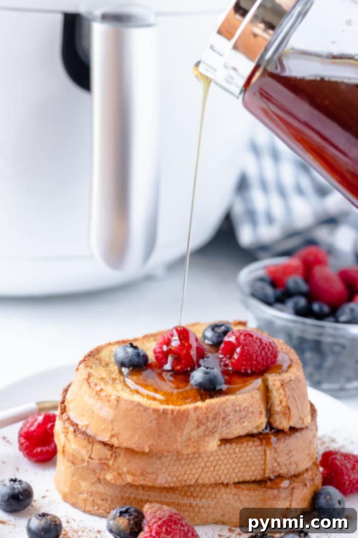 A beautifully presented stack of air fryer French toast, adorned with fresh berries and drizzled with maple syrup, with a small bowl of extra berries in the background.