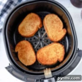 Four pieces of French toast sit perfectly toasted in an air fryer basket, with a checkered cloth nearby.
