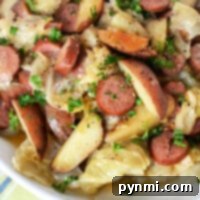 Sausage, potatoes, and perfectly seasoned crockpot cabbage blend with herbs in a bowl resting on a cloth with green and blue stripes.