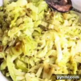 A white plate filled with slow cooker cabbage, seasoned with black pepper. A silver spoon rests on the edge of the plate.