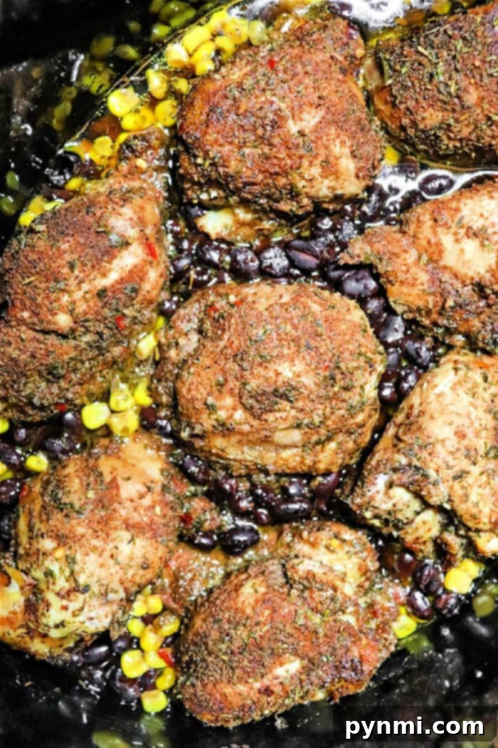 Perfectly cooked jerk chicken thighs in a crockpot, surrounded by corn and black beans, ready to serve.