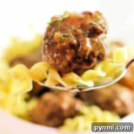 A fork with juicy crockpot meatballs and noodles, garnished with fresh herbs, stands out against a blurred background.