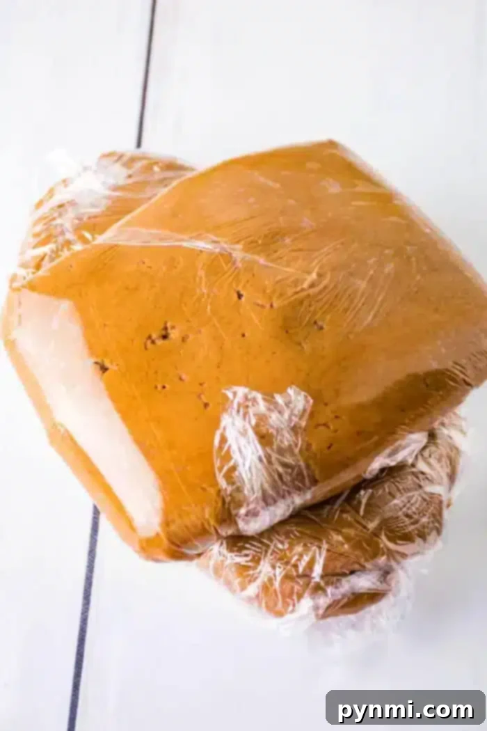 Three stacks of gingerbread dough wrapped in clear plastic wrap are placed on a white surface.