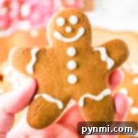 A hand holding a smiling gingerbread cookie crafted from rich gingerbread dough, adorned with delicate white icing decorations.