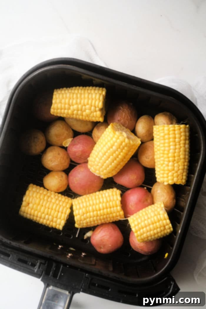 Air Fryer Seafood Boil Twist 4 Close-up of seasoned potatoes and corn cooking in a Ninja Foodi air fryer basket, showing the staggered cooking process.