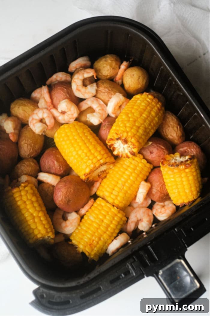 Air Fryer Seafood Boil Twist 6 Delicious seasoned shrimp cooking in an air fryer basket, turning pink and succulent, ready to be tossed with potatoes and corn.