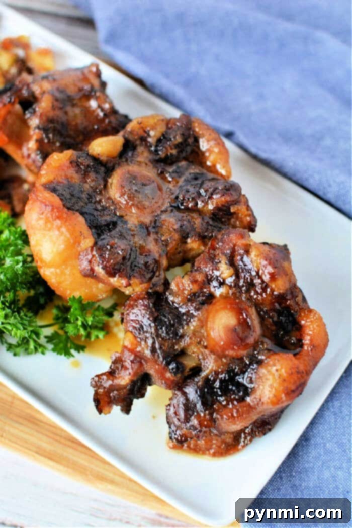 Fall-Off-The-Bone Slow Cooker Oxtail 2 Close-up of oxtail pieces on a white plate, garnished with fresh parsley. This dish captures the rich flavors reminiscent of slow cooker oxtail perfection.
