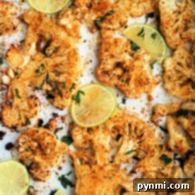 Roasted cauliflower steak slices, expertly spiced and air-fried to perfection, garnished with lime and herbs on a pristine white surface.