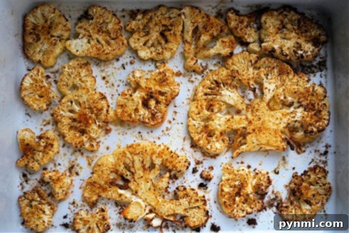 Two golden-brown air fryer cauliflower steaks garnished with fresh herbs and a lime wedge.