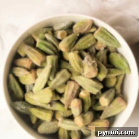 A bowl of frozen okra pieces sits on a light surface with a white cloth nearby, ready for their transformation in the air fryer.