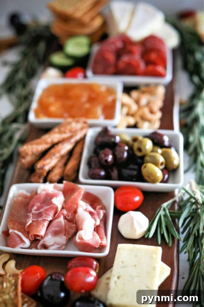 Close-up of a rustic charcuterie board with various cheeses, olives, and grapes, garnished with rosemary
