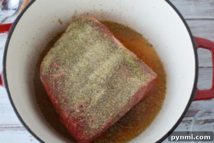 A close-up of a partially cooked frozen roast in a Dutch oven with visible broth and seasonings.