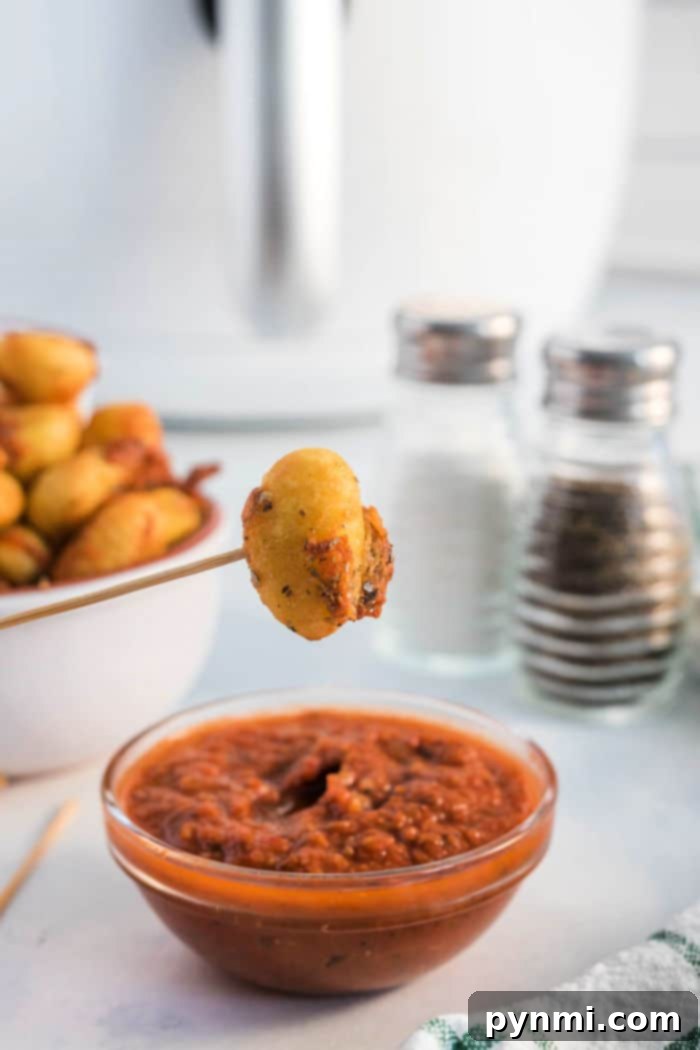 A bowl of freshly air-fried pizza gnocchi, coated in melted cheese and herbs, with marinara sauce for dipping.