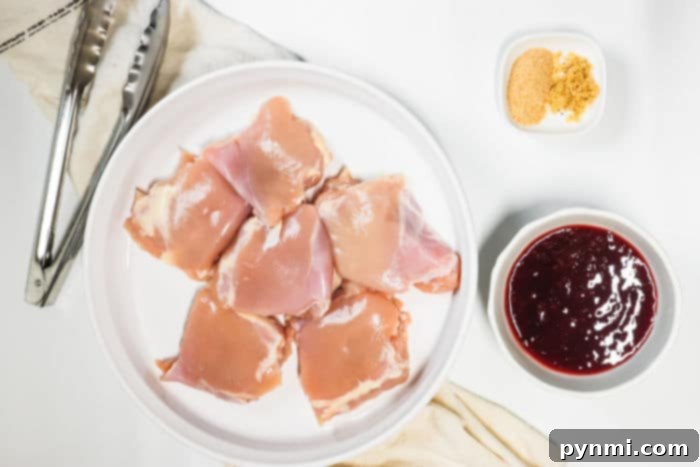 Raw chicken thighs rest on a plate, ready to transform into slow cooker BBQ perfection. Nearby, tangy sauce and savory seasonings await their turn, next to a pair of tongs resting on a cloth.