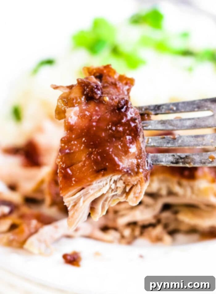 A fork holds a succulent piece of juicy, glazed pulled pork, with fresh greens blurred in the background—reminiscent of the mouthwatering tenderness found in slow-cooked BBQ chicken thighs.