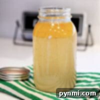 Glass jar of light brown bone broth sits on a green striped cloth, with a metal lid beside it—a perfect result of an Instant Pot recipe.