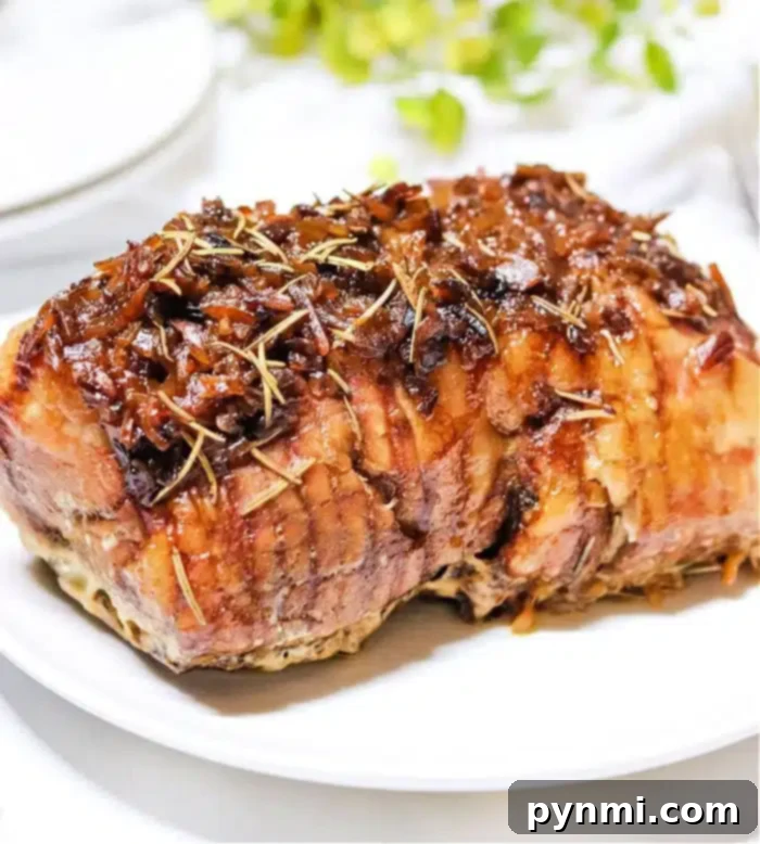 French Onion Slow Cooker Pork Roast 8 A cooked roast beef garnished with herbs and caramelized onions sits on a white plate, reminiscent of a hearty slow cooker pork roast. The meat appears juicy and is browned on the outside. In the background, there are hints of greenery and a blurred white object.